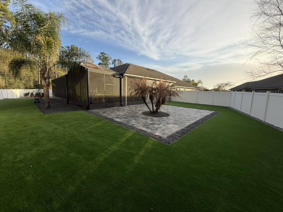 Complete backyard transformation with artificial turf and central paver pad under a dramatic sky