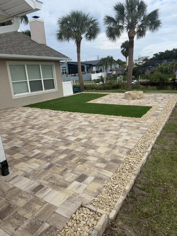 Designed backyard combining paver patio, inset turf panel, and firepit on a waterfront lot